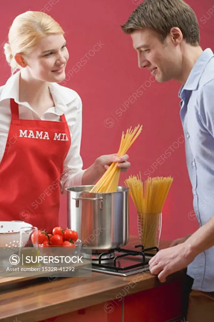 Couple cooking spaghetti with tomatoes