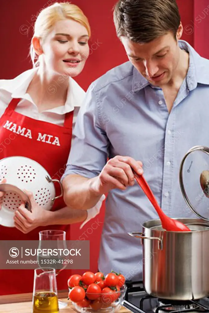 Couple cooking spaghetti with tomatoes