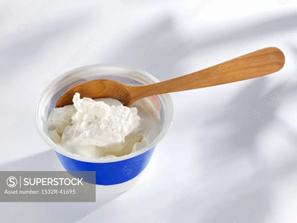 Ricotta in plastic tub with wooden spoon