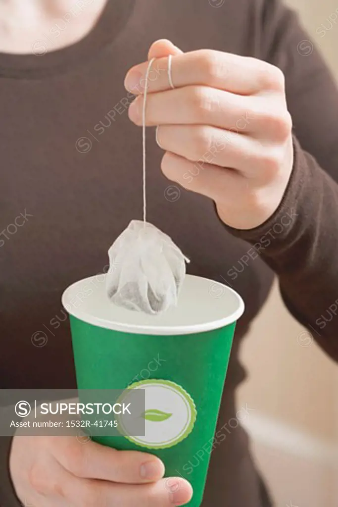 Woman holding a tea bag over a paper cup