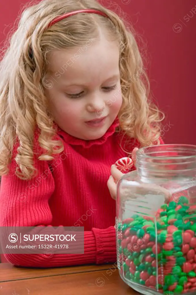 Small girl holding peppermint, jar of chocolate beans