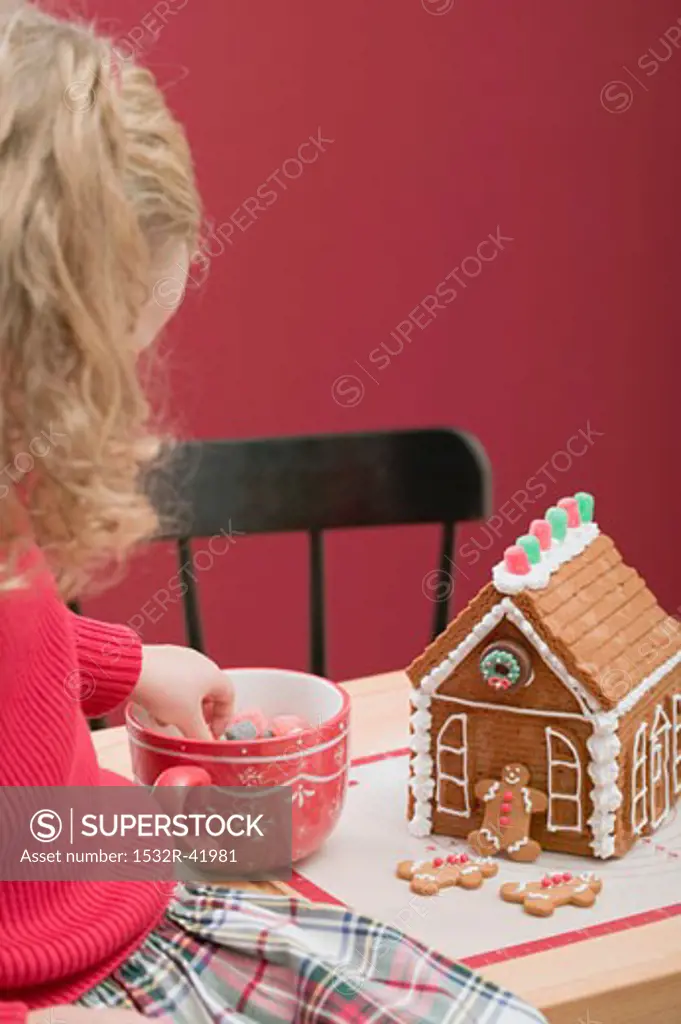 Small girl decorating gingerbread house with jelly sweets