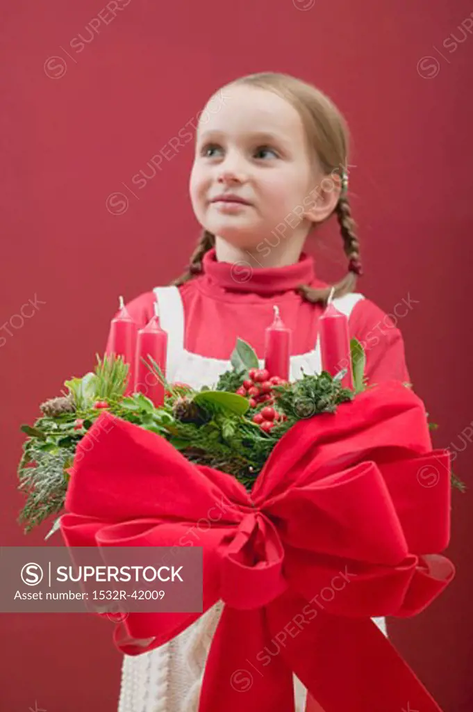 Small girl holding Advent wreath with red bow