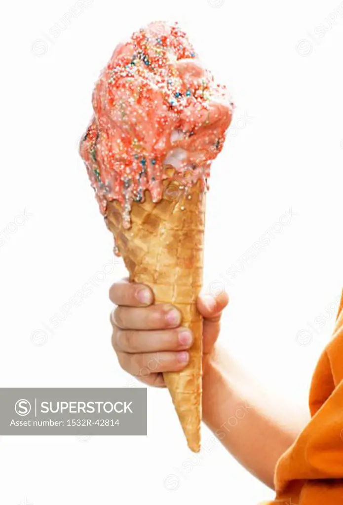 Child's hand holding large cone of strawberry ice cream