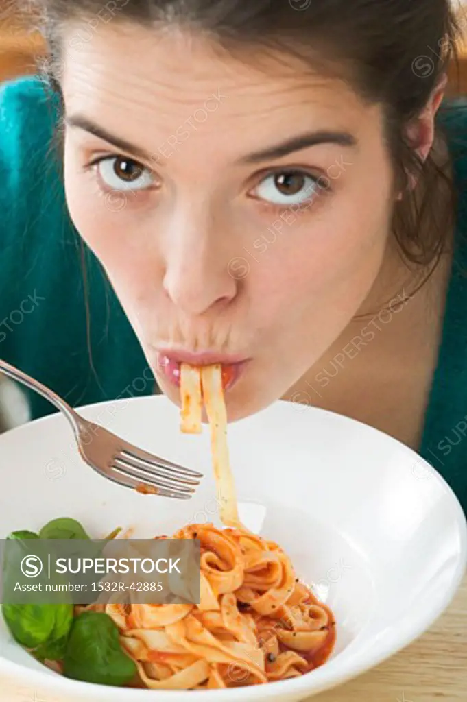 Young woman eating ribbon pasta with tomato sauce