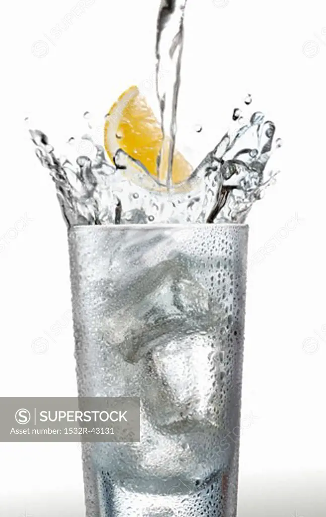 Pouring water into a glass with a wedge of lemon