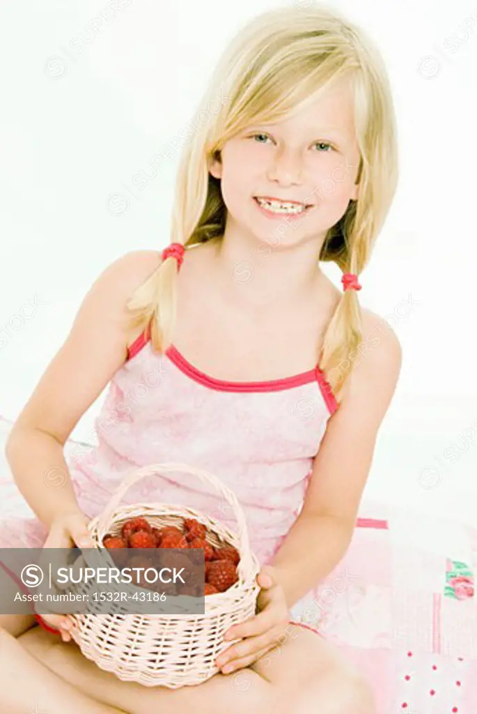 Blond girl holding small basket of fresh raspberries