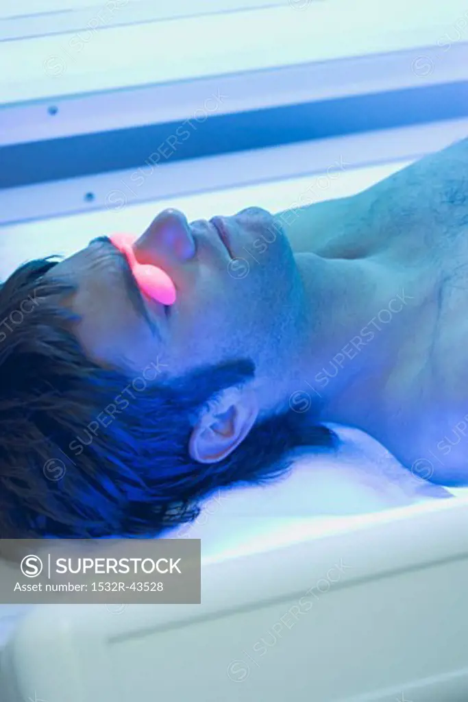 Young man in tanning goggles lying on tanning bed