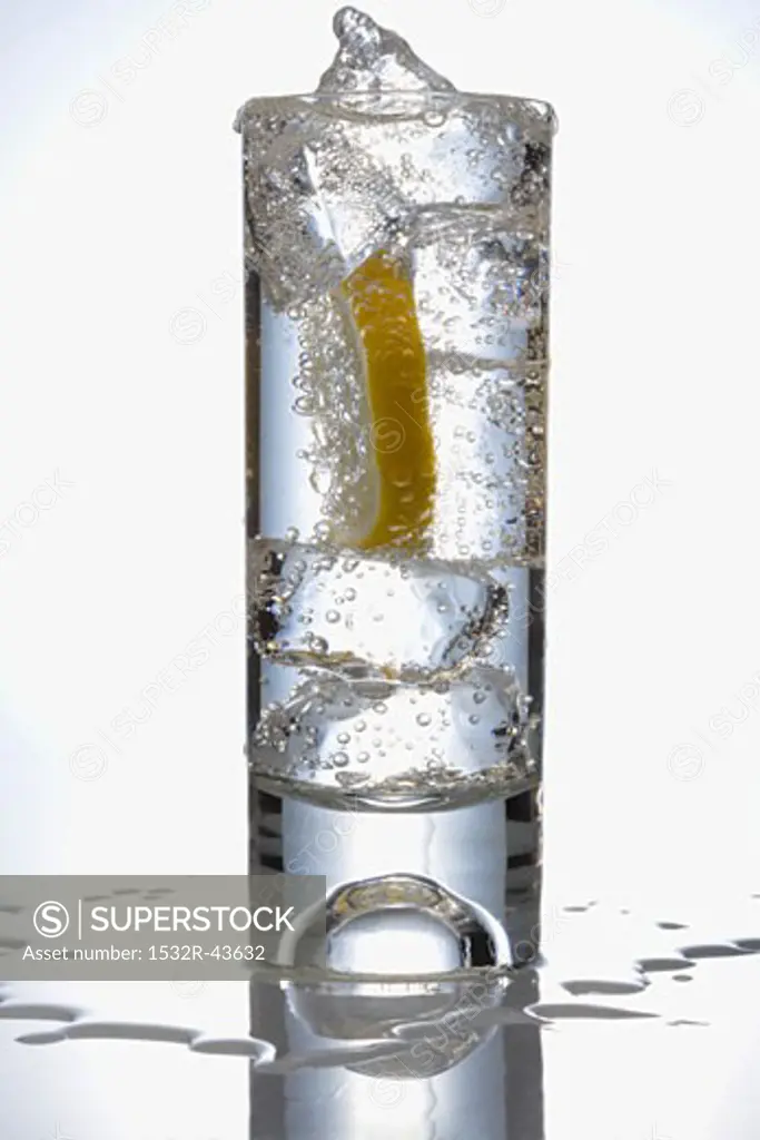Overfilled glass of water with ice cubes & slice of lemon