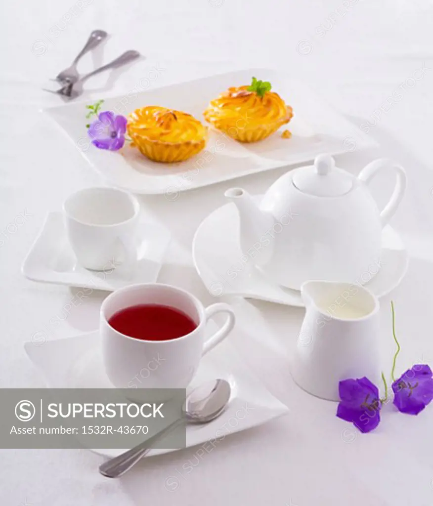 A cup of fruit tea, tea things and small cakes