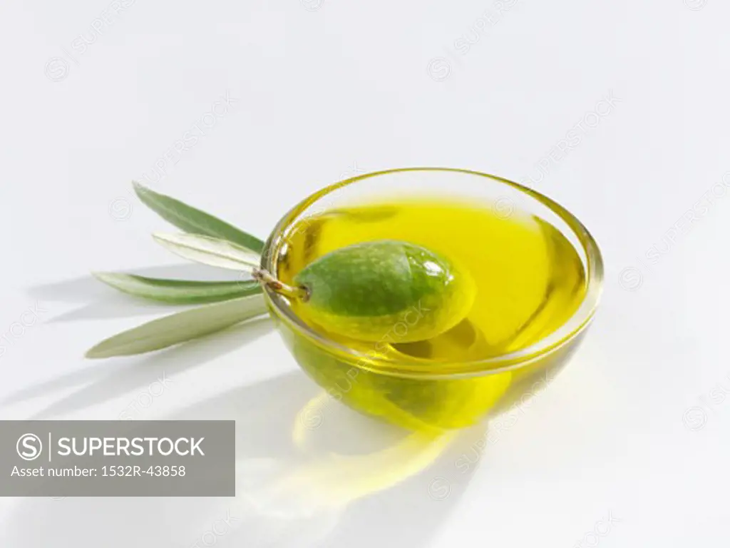 A green olive in a small glass dish of olive oil