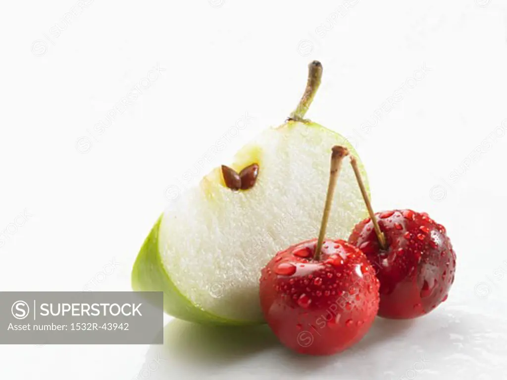 Wedge of green apple and two cherries with drops of water