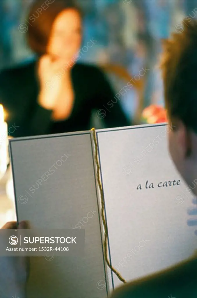 Man reading menu in restaurant with woman in background