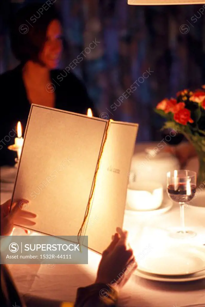 Guest reading menu in restaurant with woman in background