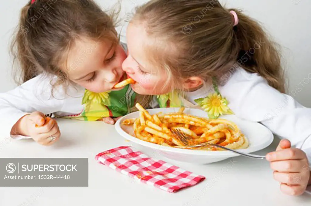 Two girls eating macaroni with tomato sauce