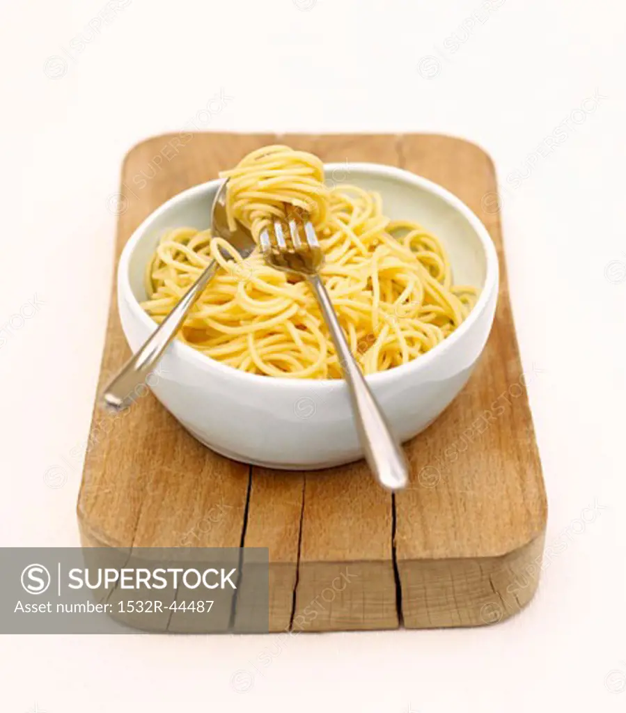 Bowl of cooked spaghetti on a wooden board