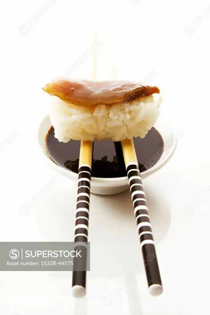 Nigiri sushi on chopsticks on small bowl of soy sauce