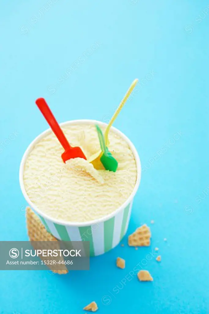 A tub of vanilla ice cream with three plastic spoons