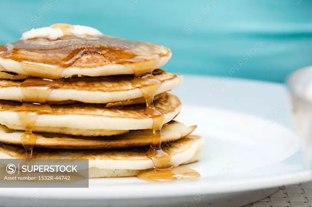 Maple syrup running down a pile of pancakes with butter