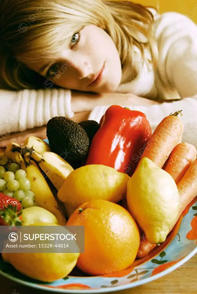 Young woman sitting in front of plate of fruit & vegetables
