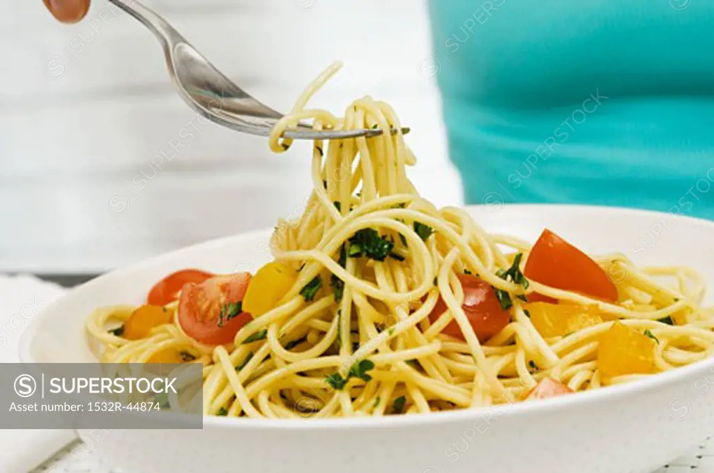 Picking up spaghetti with herbs and vegetables on a fork