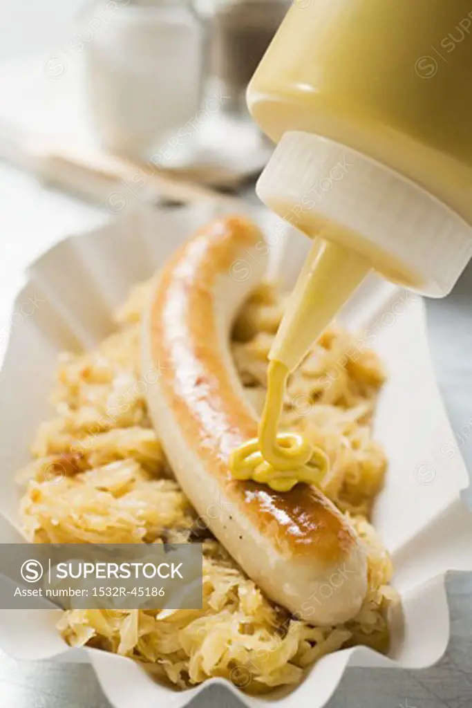 Putting mustard on sausage with sauerkraut