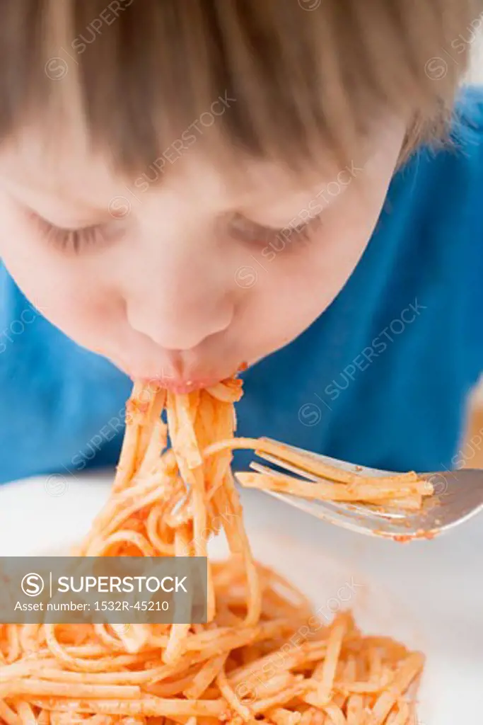 Small boy eating noodles with tomatoes