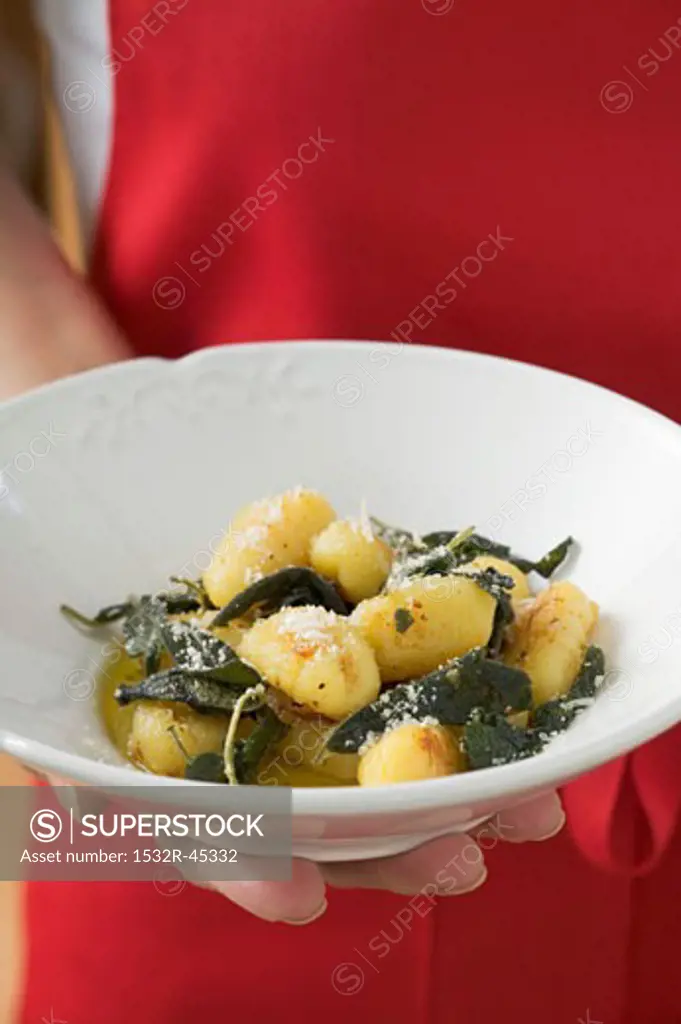Hand holding plate of gnocchi in sage butter
