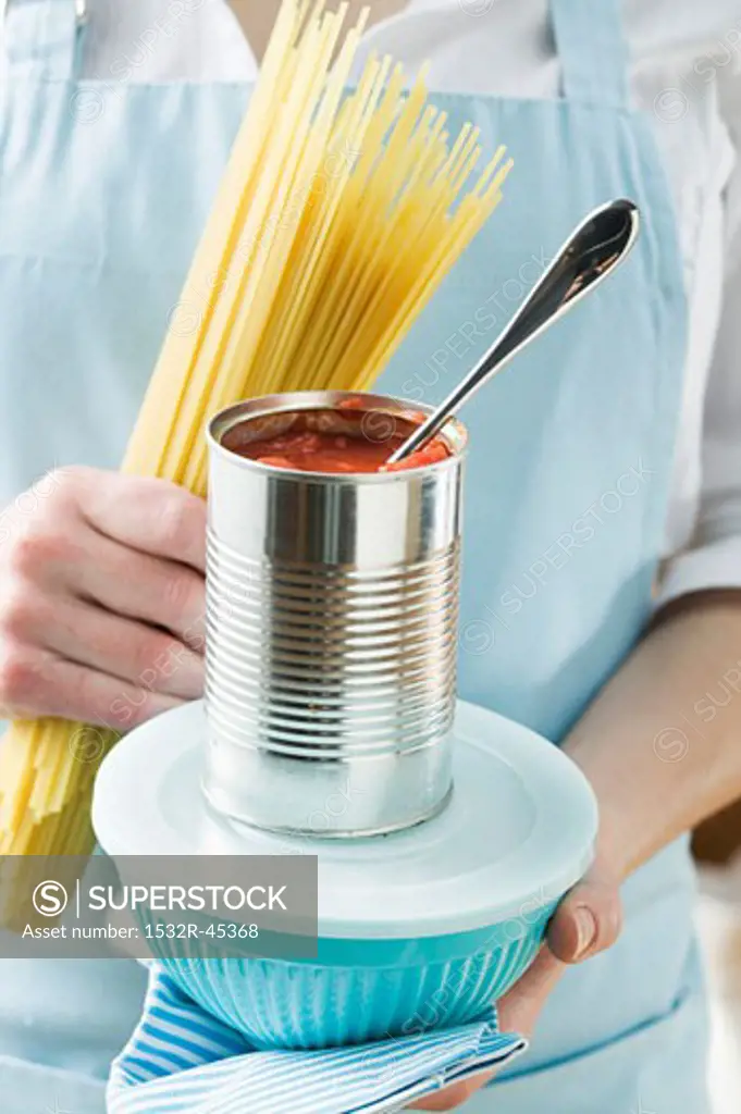 Woman holding spaghetti, tin of tomatoes & food container