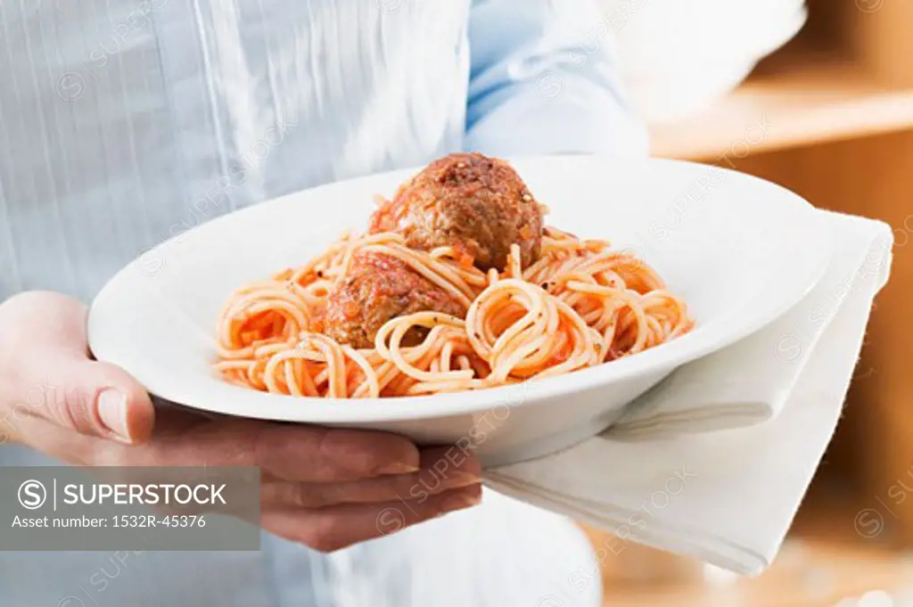 Person holding plate of spaghetti with meatballs