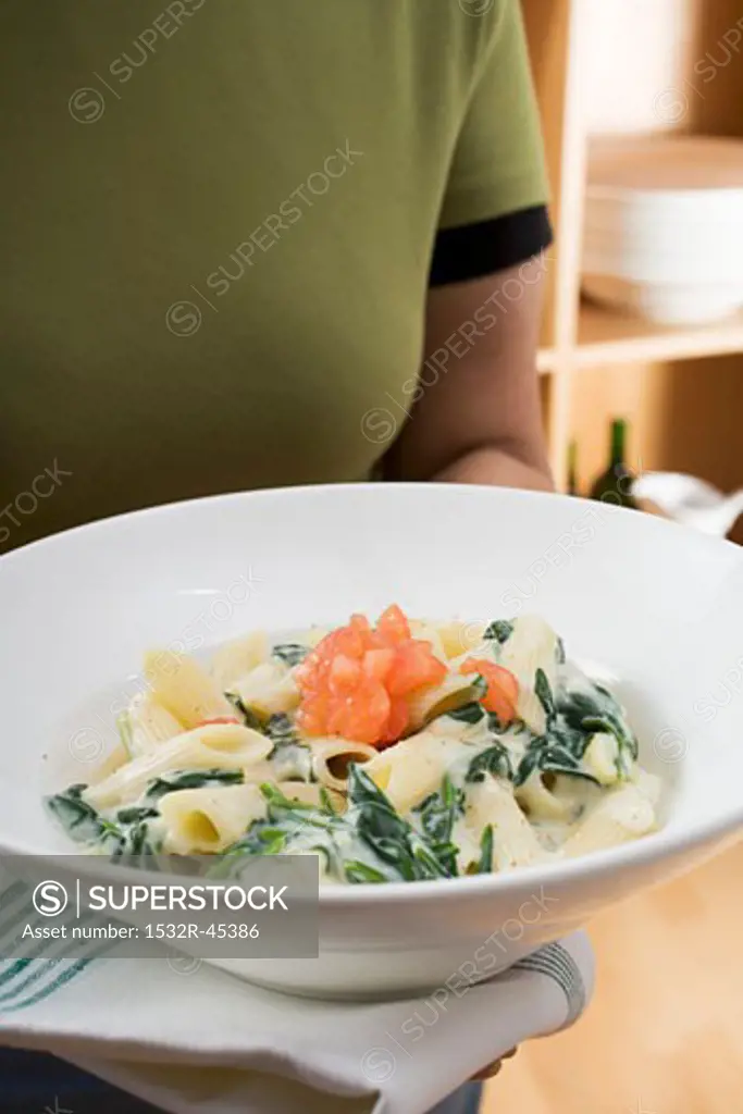 Woman holding plate of penne with spinach and tomatoes