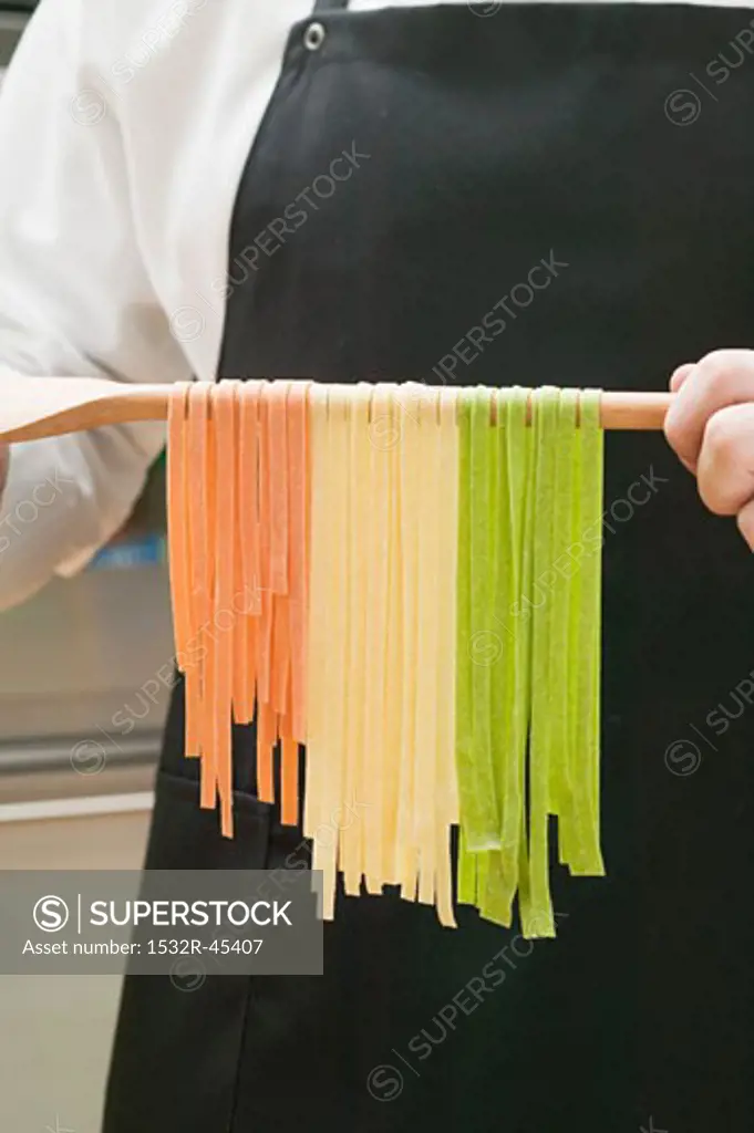 Home-made ribbon pasta hanging over wooden spoon