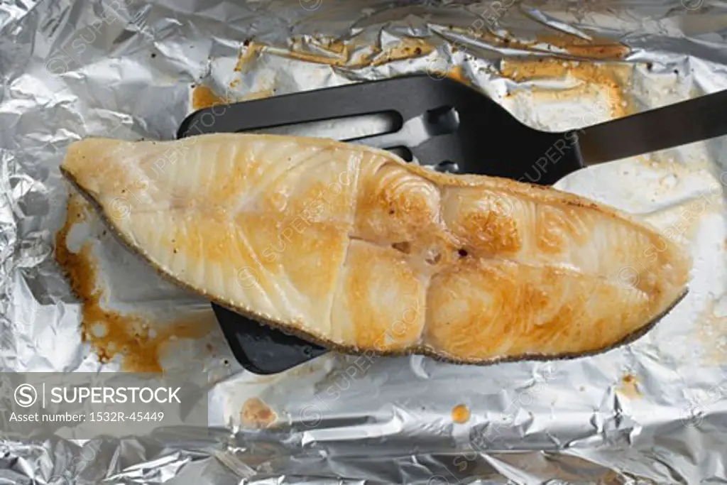 Grilled cod steak on aluminium foil with spatula