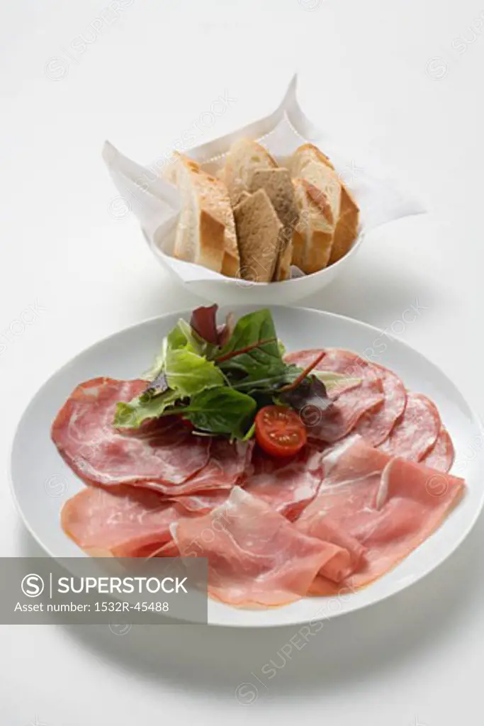 Raw ham and salami on plate, baguette slices