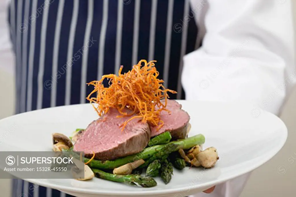 Chef serving beef fillet with green asparagus
