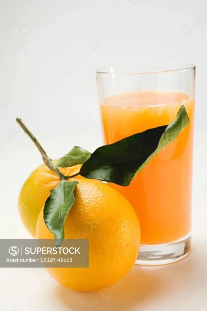 Glass of orange juice and two oranges with leaves