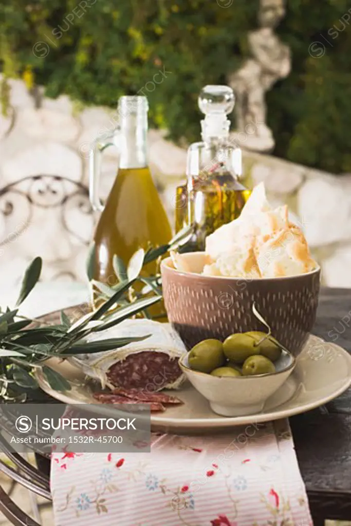 Olives, salami, crackers & olive oil on table out of doors