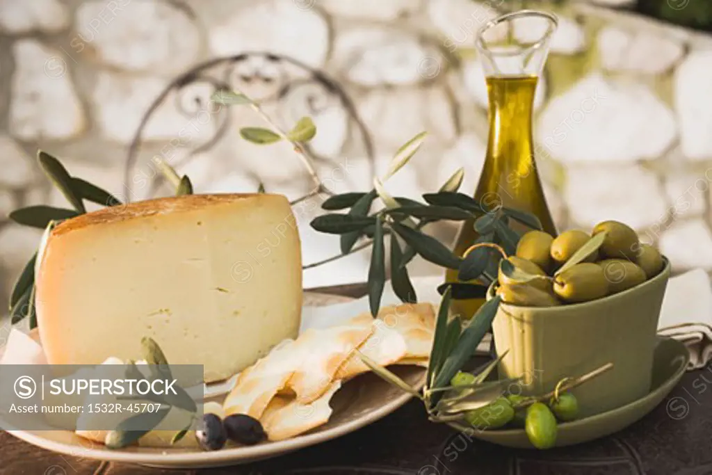 Olives, cheese, crackers & olive oil on table out of doors