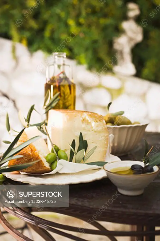 Cheese, olives and olive oil on table out of doors