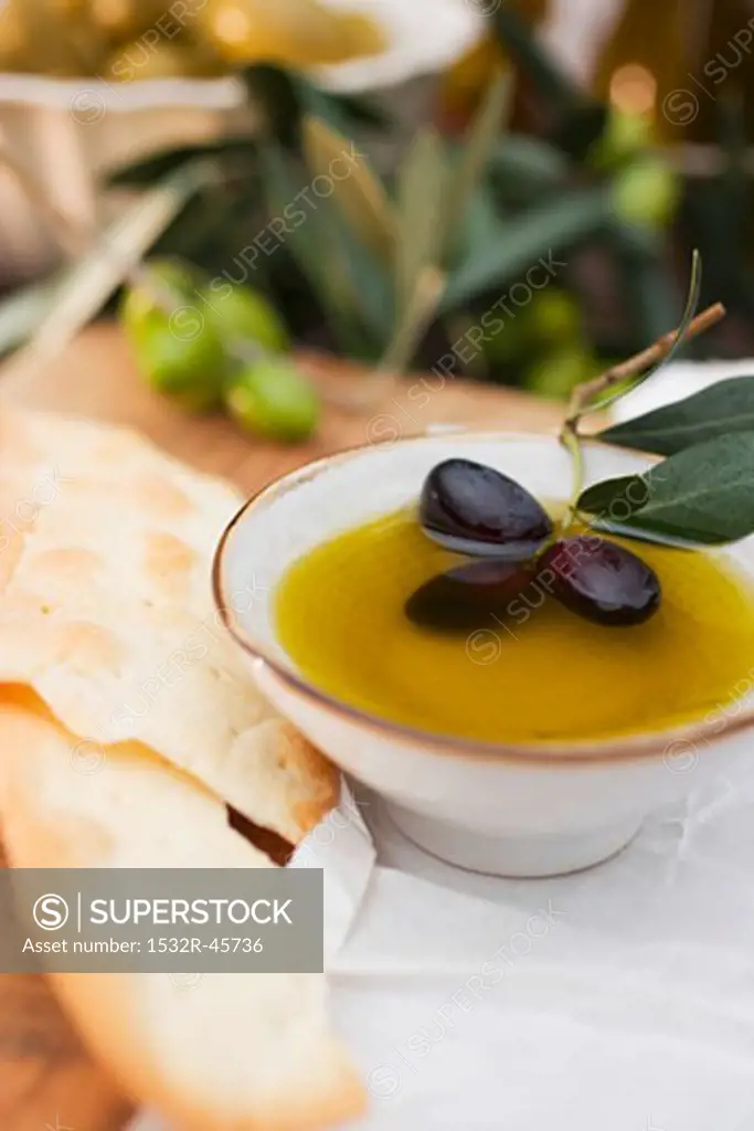 Olive oil in bowl with black olives, crackers beside it