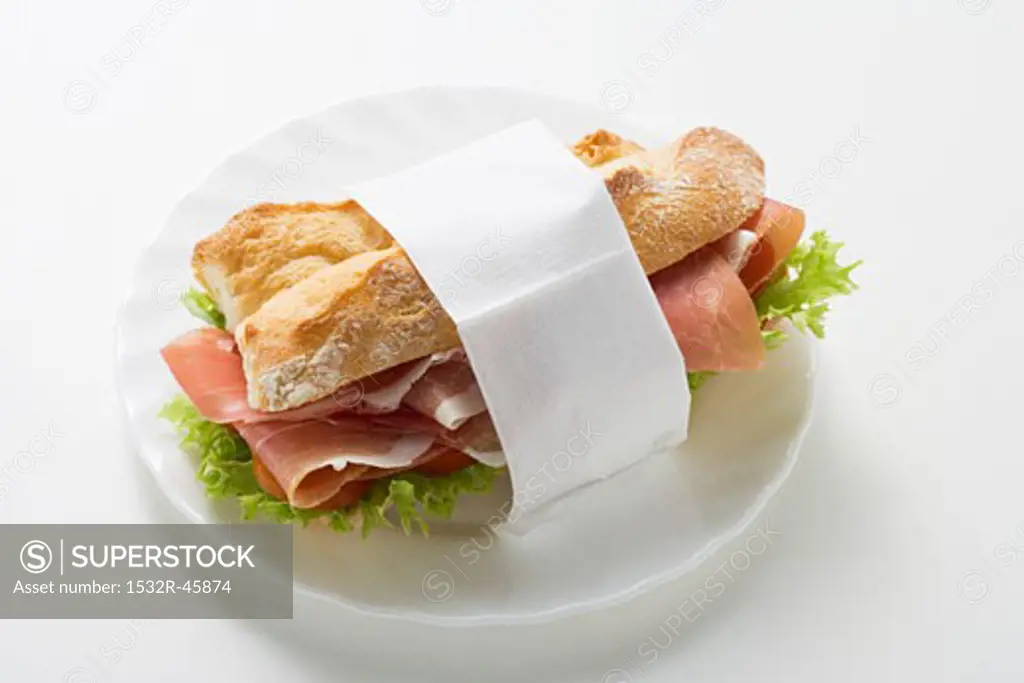 Raw ham sandwich in paper napkin on plate
