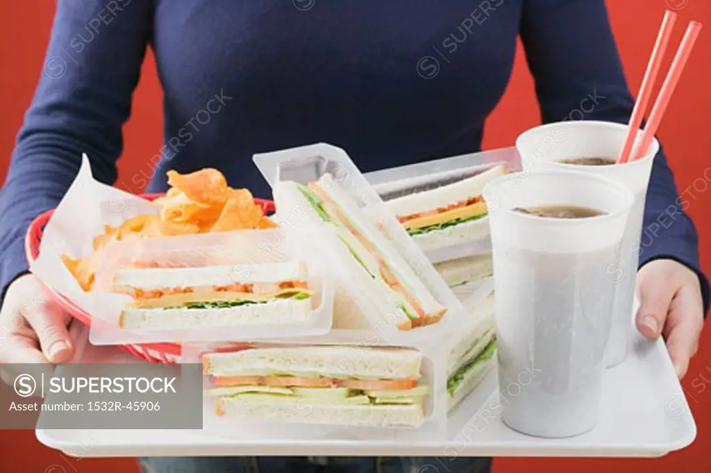 Woman holding sandwiches, cola and crisps on tray