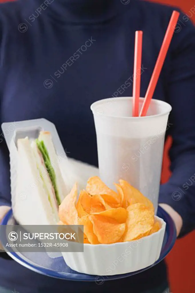 Woman holding sandwich, cola and crisps on tray