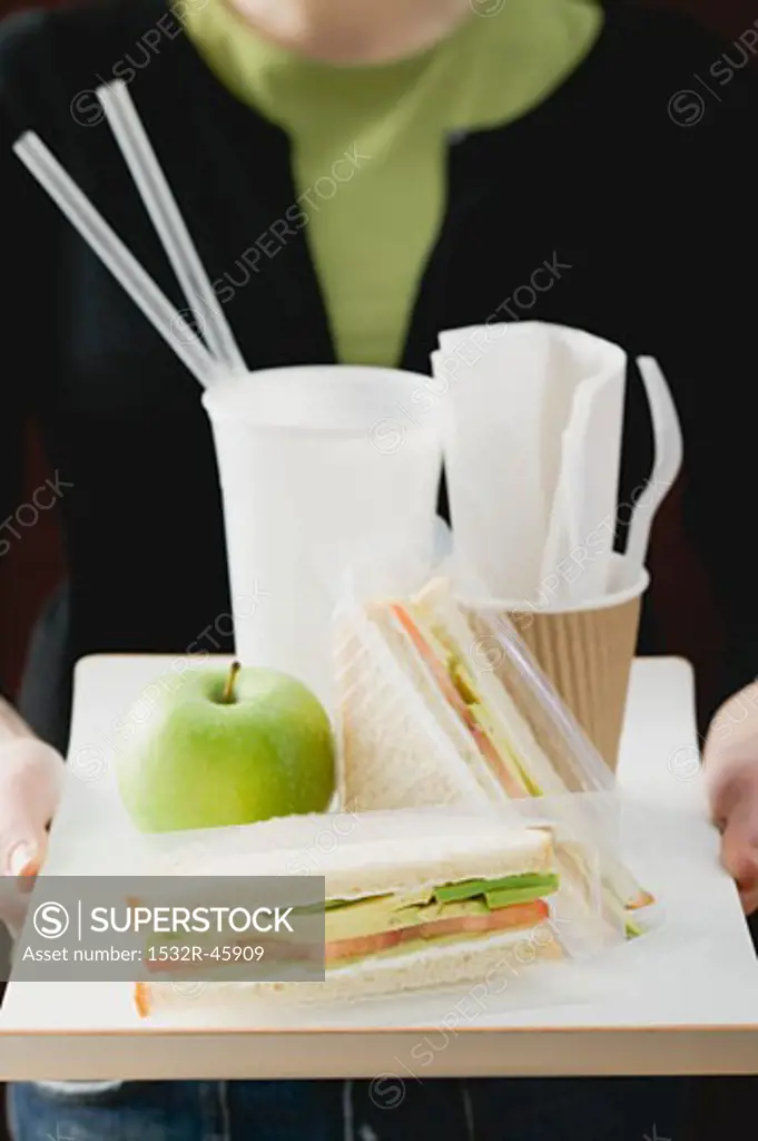 Woman holding sandwiches, apple and drink on tray
