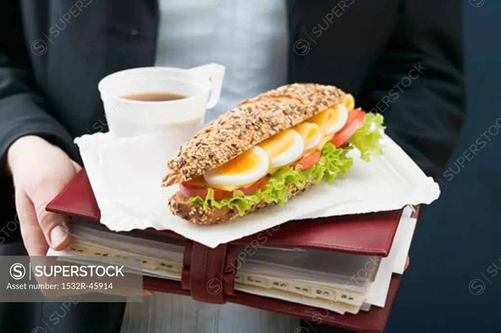 Woman holding sandwich and drink on organiser