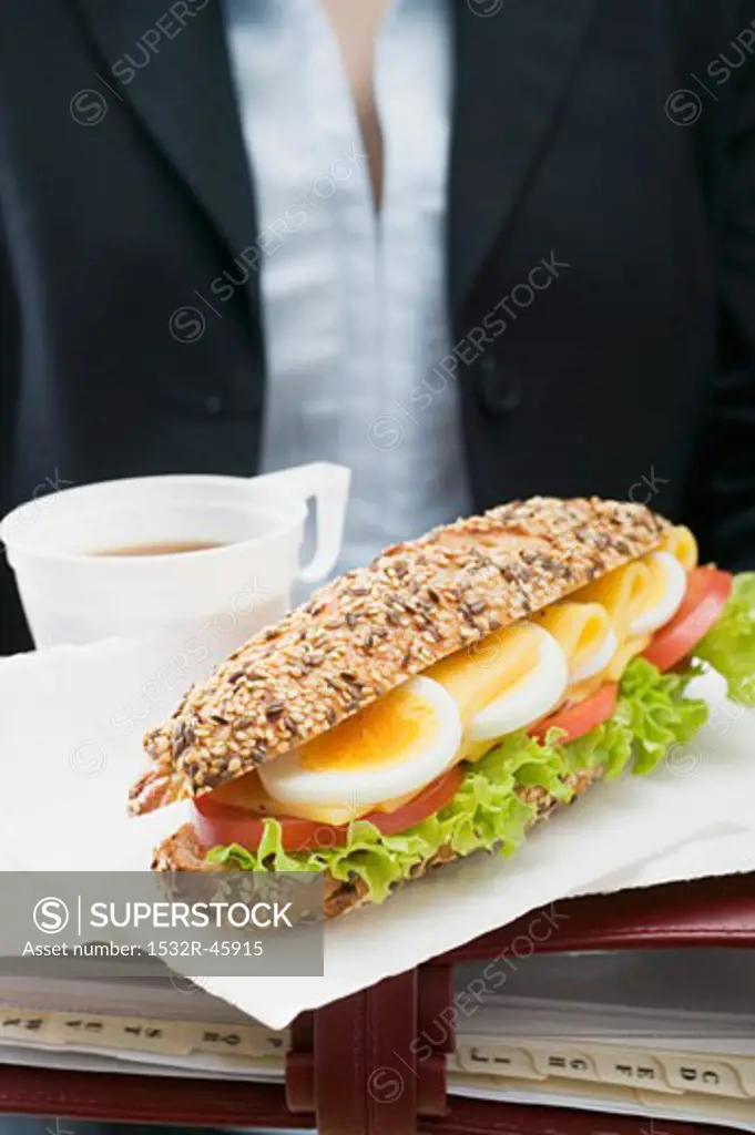 Woman holding sandwich and drink on organiser