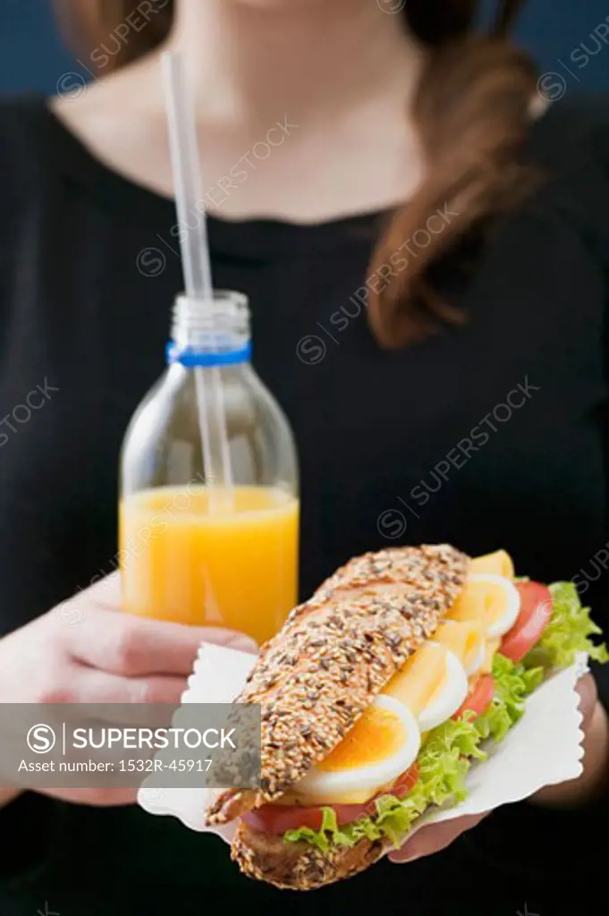 Woman holding sandwich and bottle of orange juice