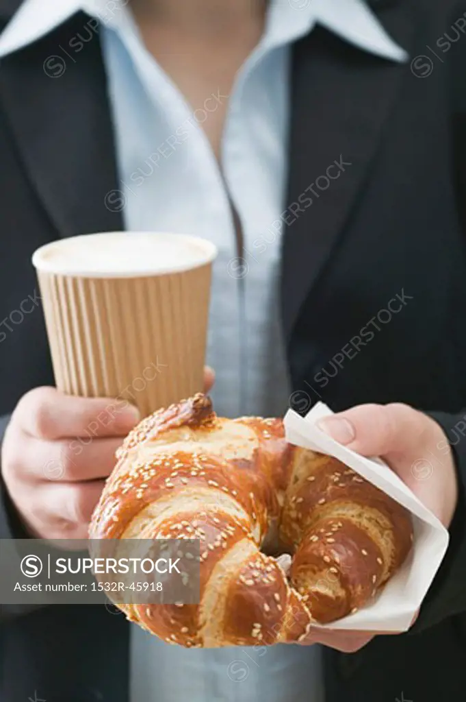 Woman holding pretzel-style croissant & coffee in plastic cup