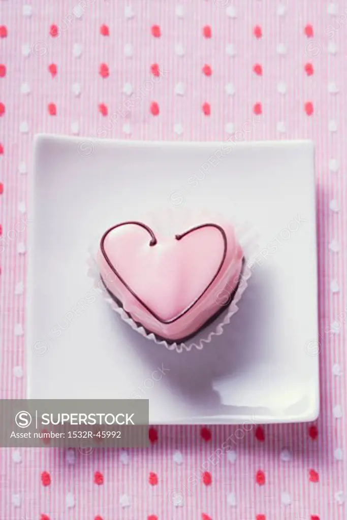 Pink heart-shaped petit four on plate (overhead view)