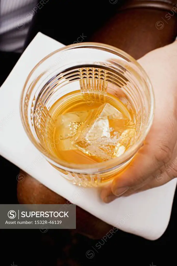 Hand holding glass of whisky with ice cubes